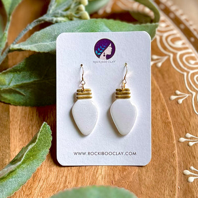 Handmade Christmas earrings featuring elegant white clay and gold accents on a display card with greenery background.